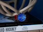 MONTAUK CHRONO men's watch styled on art books — blue chronograph dial with red leather strap, still-life product photo