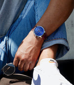 MONTAUK CHRONO men's watch on wrist with jeans and sunglasses — casual lifestyle photo, blue dial with red-brown leather strap